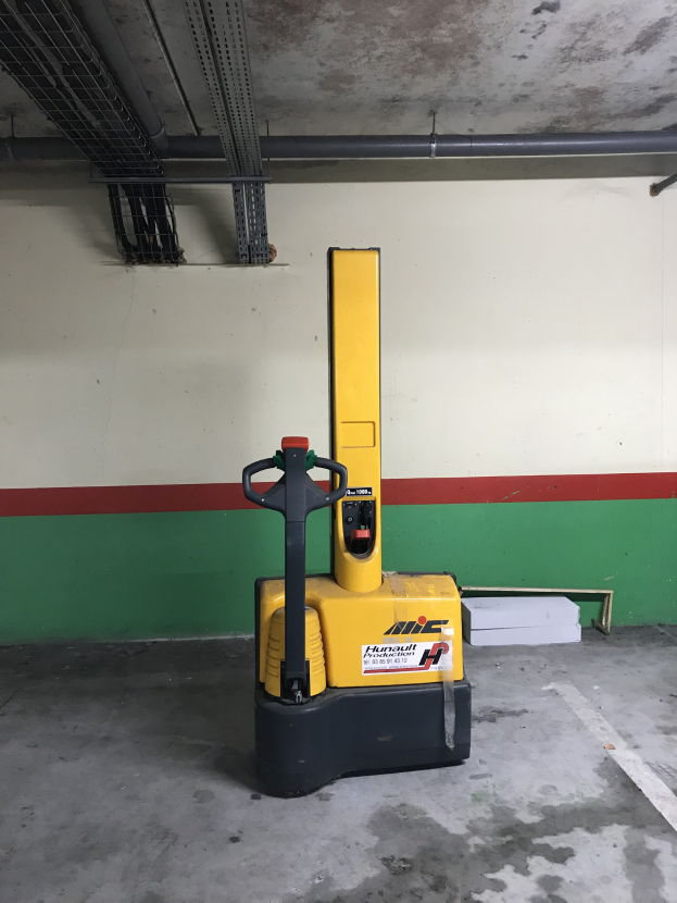 Ein gelber Gabelstapler in einem Lagerhaus mit Metallregalen auf der linken Seite und einer Wand im Hintergrund.