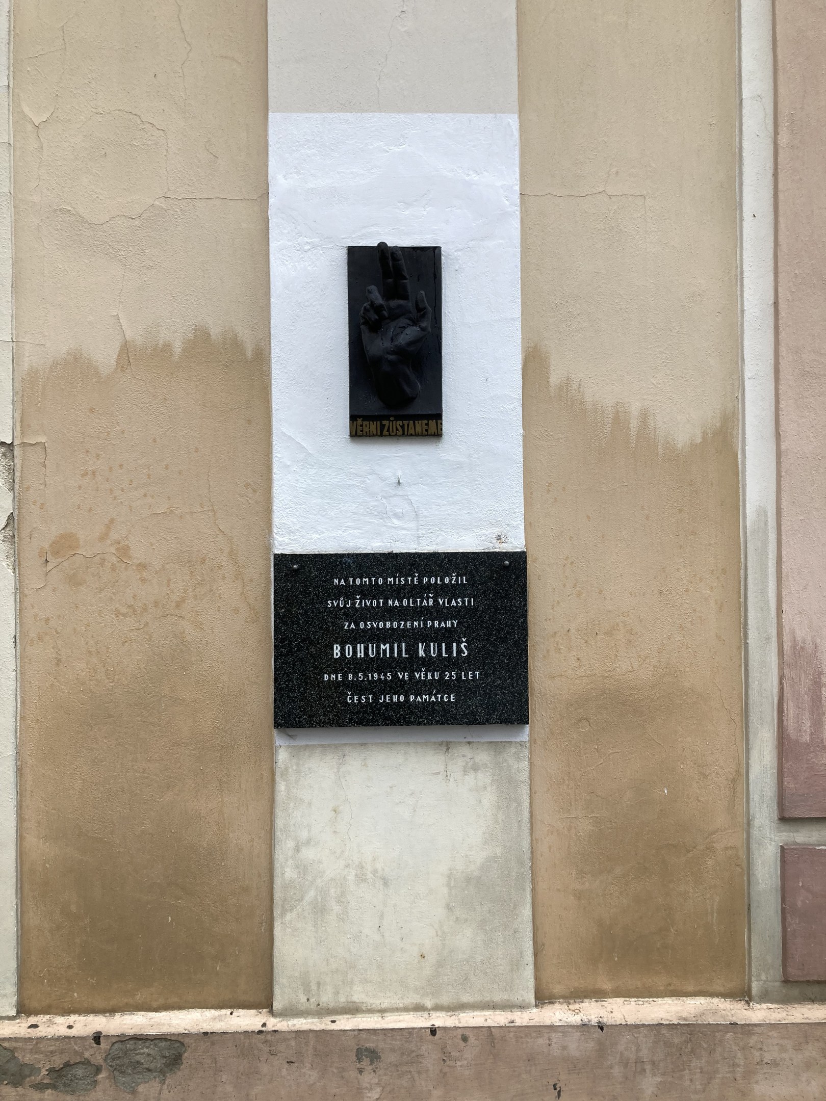 Schwarze Tafel an einem Gebäude mit einer darauf liegenden Hand, beschriftet mit Text, wahrscheinlich ein Holocaust-Mahnmal.