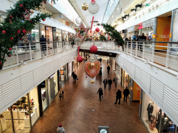 Ein Einkaufszentrum im Weihnachtslook mit Menschen, die umherlaufen, Schaufensterpuppen in festlicher Kleidung, Geschäften, Geländern und Lichtern, die eine gemütliche Atmosphäre schaffen.