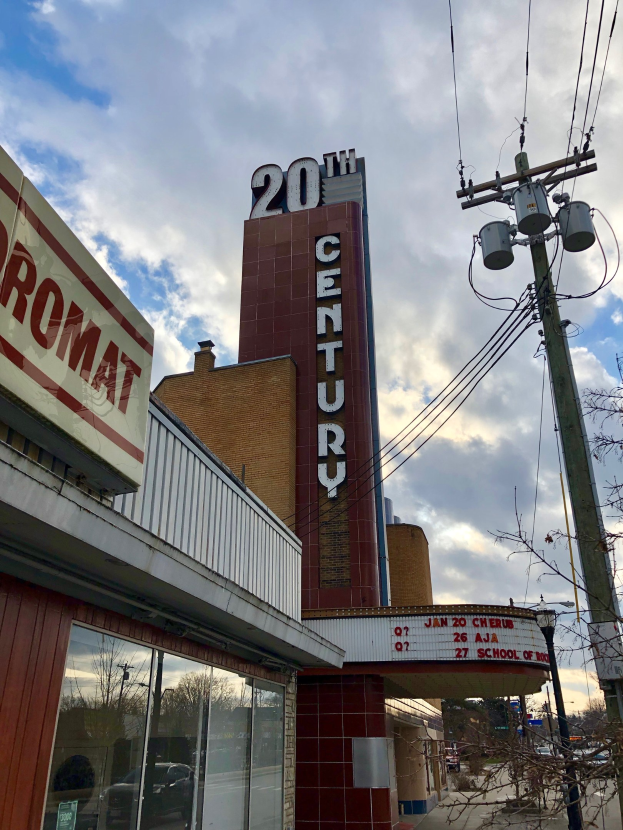 Außenansicht des 20th Century Theatre in Detroit, Michigan, mit Glaswänden und Beschriftung, umgeben von Bäumen, Strommasten und Drähten, mit einem bewölkten Himmel im Hintergrund.