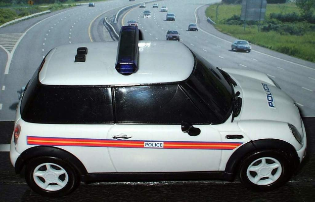 Weißer Polizeiwagen mit der Aufschrift "Polizei" auf einer Landstraße, umgeben von fahrendem Verkehr, Gras und Bäumen auf beiden Seiten.