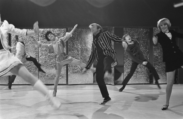 Eine Gruppe von Menschen, die auf einer Bühne tanzen, mit einer Wand im Hintergrund, alle in Schwarz-Weiß, mit Schuhen.