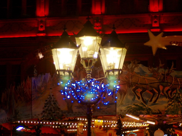 Eine Straßenlaterne mit dekorativen Lichtern und Gegenständen, die vor einem Stadtgebäude in der Nacht zu sehen ist.