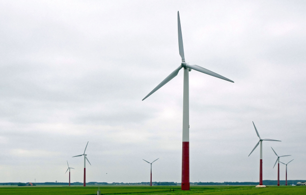 Eine Gruppe hoher weißer Windräder in einer grünen Landschaft mit Bäumen und Wolken im Hintergrund.