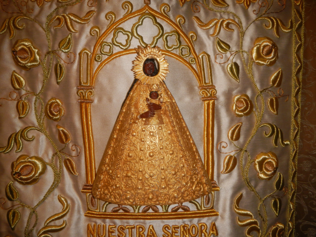 Goldverzierte Chasuble mit einer serenen Frau in einem hochgeschlossenen, langärmeligen Kleid mit einem Dutt, umgeben von kunstvollen Texten und goldenen Verzierungen.