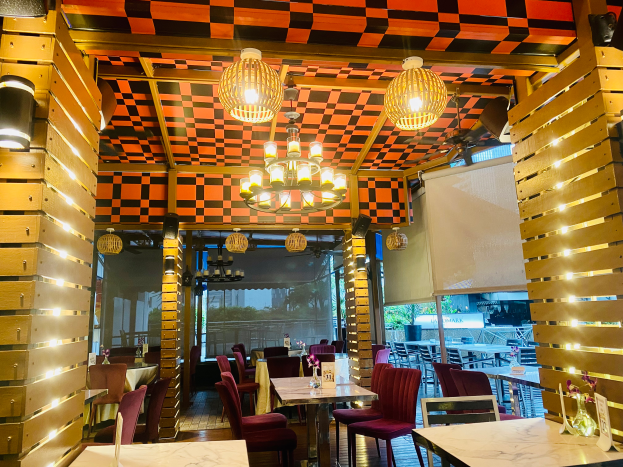 Ein Restaurant-Innenraum mit Tischen und Stühlen unter einer karierten Decke, dekoriert mit Blumenvasen und anderen Gegenständen, und Wänden, die mit Lichtern und Kronleuchtern geschmückt sind.