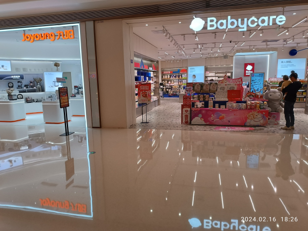 Babycare-Laden im Mall of Asia mit Regalen voller Artikel, Schildern, einem Display, Deckenleuchten und einer Gruppe von Menschen umgeben von Spielzeugen.
