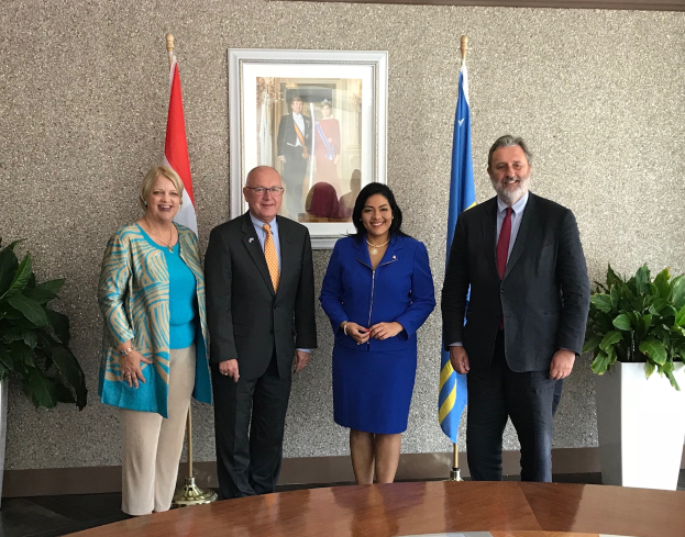 Eine Gruppe lachender Menschen um einen Tisch mit Papieren stehend, umgeben von Fahnen, Topfpflanzen und einem Foto auf der Wand, feiern die Unterzeichnung eines Memorandums zwischen den Vereinigten Staaten und Kanada.