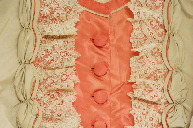 Nahaufnahme eines rosafarbenen und cremefarbenen Kleides mit weißer Spitze und Knöpfen vorne.