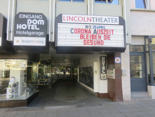 Außenansicht des Lincoln Theaters in Berlin, Deutschland, mit Glasfenstern und -türen und einer Tafel, die eine belebte Stadtkulisse im Inneren zeigt.