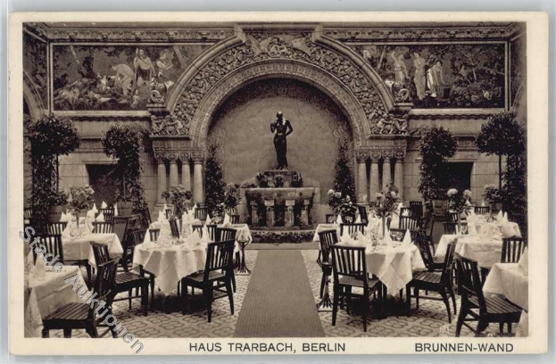 Schwarzes und weißes Foto eines alten Berliner Restaurant-Interieurs mit Tischen, die mit Vasen, einer Statue im Hintergrund, geschnitzten Wänden und Text unten dekoriert sind.
