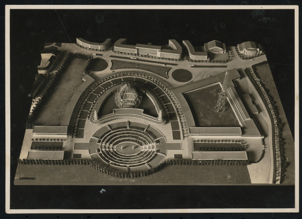 Schwarzes und weißes Rahmenfoto eines detaillierten Modellkonzertsaals mit einer großen zentralen Kuppel, Steinwänden, Metalldach und einer hell erleuchteten Bühne, die von einer Menge umgeben ist.