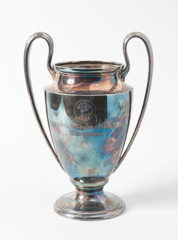 Der UEFA-Champions-League-Pokal, eine stählerne Tasse mit zwei Griffen und einem blauen und silbernen Farbschema, geprägt mit 'UEFA Champions League', vor einem weißen Hintergrund dargestellt.