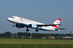 Ein Airbus A320-200 der Austrian Airlines startet vom Frankfurter Flughafen, mit grünem Gras, Bäumen, Gebäuden und einer Kontrollturm im Hintergrund.