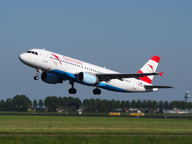 Ein Airbus A320-200 der Austrian Airlines startet vom Frankfurter Flughafen, mit grünem Gras, Bäumen, Gebäuden und einer Kontrollturm im Hintergrund.