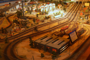 Eine detaillierte Modellbahnausstellung in einem Museum, die Gebäude, Bäume, Eisenbahnschienen, Fahrzeuge, Pfosten, Lichter und andere Gegenstände umfasst, die eine belebte Stadtlandschaft nachahmen.