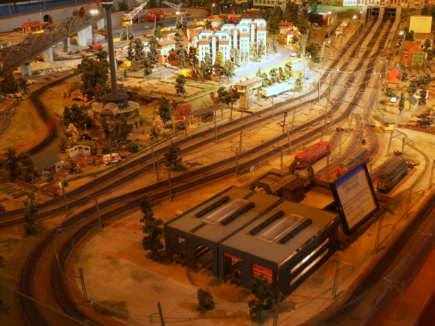 Eine detaillierte Modellbahnausstellung in einem Museum, die Gebäude, Bäume, Eisenbahnschienen, Fahrzeuge, Pfosten, Lichter und andere Gegenstände umfasst, die eine belebte Stadtlandschaft nachahmen.