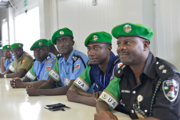Gruppe von Polizeibeamten bei einer Schulung an einem Tisch mit Mobiltelefonen und anderen Gegenständen in einem Raum mit Fenstern und Deckenleuchten.