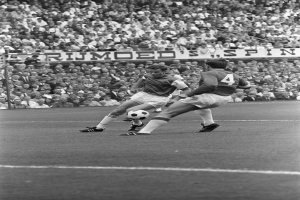 Schwarzes und weißes Foto von zwei Fußballspielern im Einsatz auf einem Feld mit Zuschauern im Hintergrund und einem Banner mit der Aufschrift "Bobby Charlton im Einsatz für Manchester United."