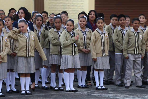 Gruppe von Kindern in Schuluniformen vor einem Gebäude mit einer Wand und einem Rollladen im Hintergrund.