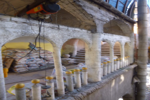 Altes Gebäude mit Bogen, Säulen und Treppen wird renoviert, mit verstreuten Werkzeugen, Materialien und Gegenständen, darunter Taschen und eine Maschine mit Drähten oben drauf.