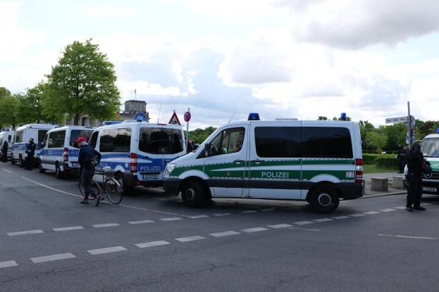 Eine Gruppe von Polizeifahrzeugen steht entlang einer Straße mit einem Radfahrer im Vordergrund und Gebäuden, Bäumen und Beschilderung im Hintergrund.