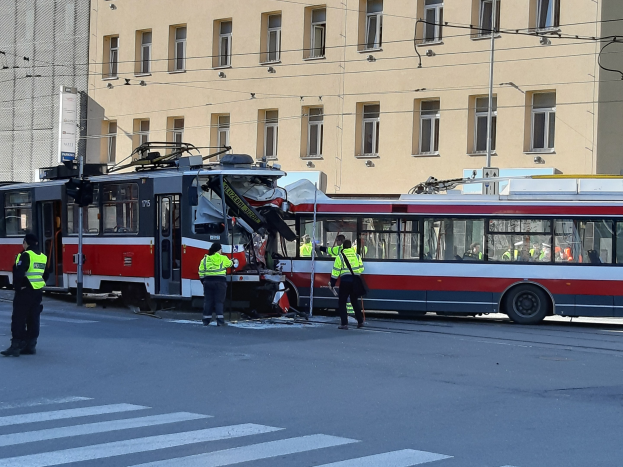 Rote und weiße Straßenbahn in einen Straßenrandunfall mit mehreren Menschen in der Nähe und einem Gebäude im Hintergrund verwickelt.