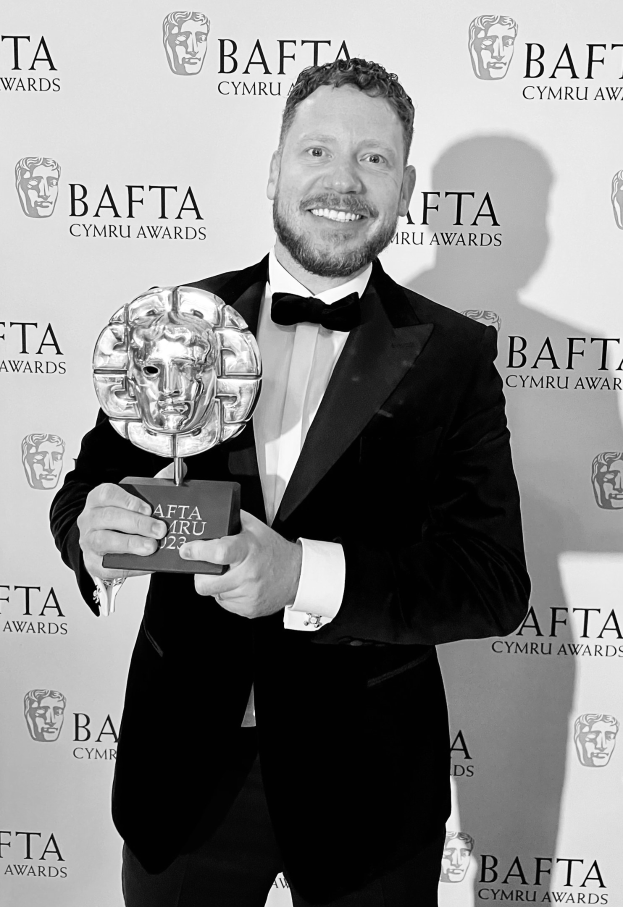 Ein Mann in einem Smoking, der eine BAFTA-Auszeichnung hält und lächelt, vor einem Hintergrund mit der Aufschrift "BAFTA Awards 2018."