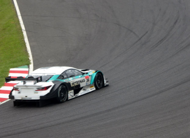 Ein silberner Mercedes-AMG GT3-Rennwagen auf einer Strecke mit Text auf seiner Karosserie und Gras links daneben.