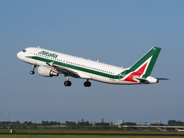 Ein Airbus A320-232 ERJ-EJZ der Alitalia startet vom Frankfurter Flughafen mit grünem Gras darunter, Bäumen und Gebäuden im Hintergrund und einem klaren blauen Himmel darüber.