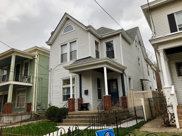 Reihe von Häusern mit Fenstern, Türen, Säulen, Geländern, Stufen und Dächern, umgeben von einem Metallzaun, Gras, Pflanzen, Bäumen und einem bewölkten Himmel; Mietschild unten mit der Adresse 5901 S Elmwood Ave, Chicago 60618.