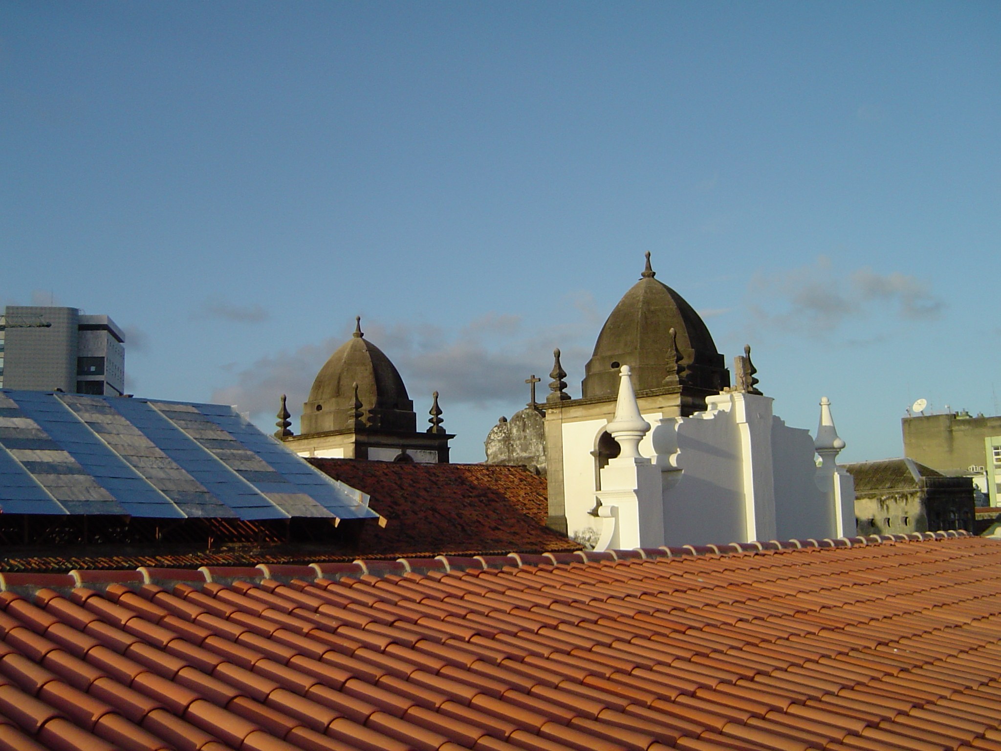 Stadtansicht mit mehreren Gebäuden im Vordergrund, einem klaren blauen Himmel im Hintergrund und Solarpanelen auf dem Dach eines Gebäudes.