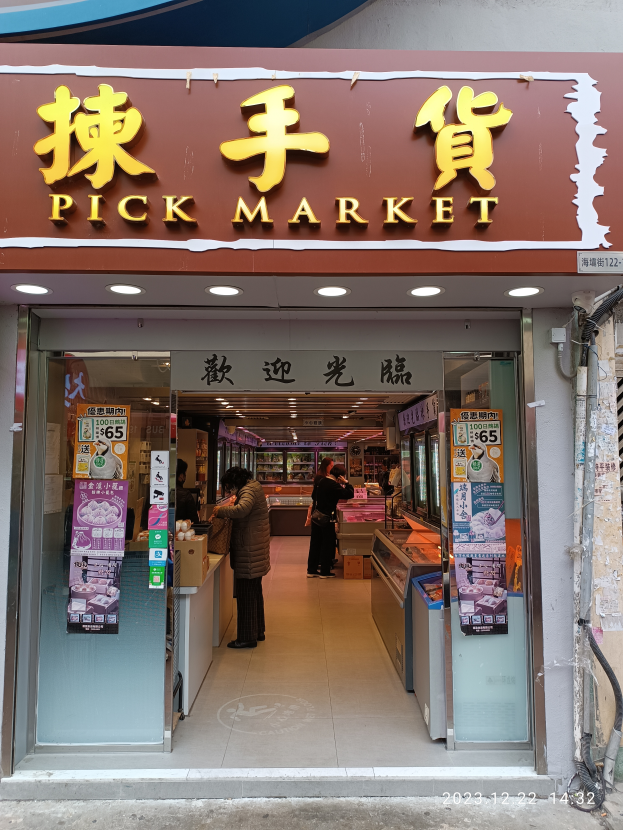 Ein Markt in Hong Kong mit ein paar Menschen davor und einer Wand mit Rohren auf der rechten Seite.