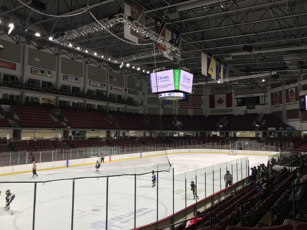 Hockey-Spiel in einer großen Arena mit einem zentralen Netz, Zuschauern auf beiden Seiten, Deckenbeleuchtung und Bannern, identifiziert als die St. Louis Blues Arena.