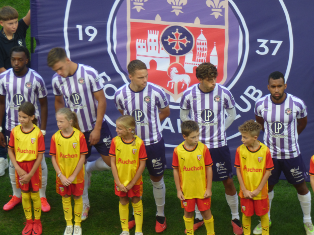 Eine Gruppe junger Menschen auf einem Fußballfeld, mit einem Banner im Hintergrund, auf dem "Preston Primary School Football Team" steht.