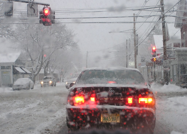 Eine ruhige, schneebedeckte Straße, gesäumt von Häusern und Bäumen mit minimalem Fahrzeugverkehr.