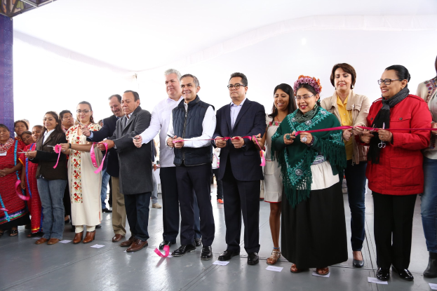 Eine Gruppe von Menschen bei einer Scherenschnitte-Zeremonie, mit Scheren haltend, mit Papieren auf dem Boden und einem weißen Tuch im Hintergrund.