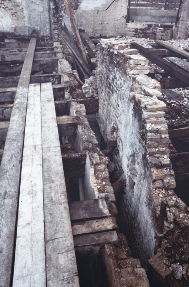 Altes Gebäude beim Abriss mit verstreuten Holzplanken und Steinen im Vordergrund, Ziegelwand im Hintergrund sichtbar.