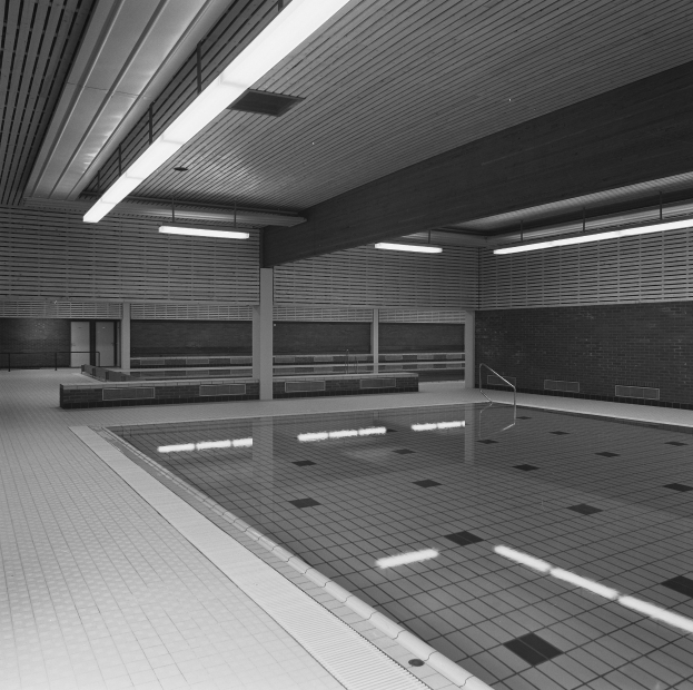 Innenpool mit klarem Wasser, gefliesten Wänden und Boden, Deckenbeleuchtung und minimalen Umgebungsgegenständen in einem großen, ruhigen Gebäude.