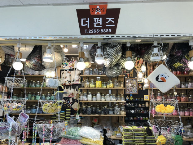 Ein unordentlicher Laden in Seoul, der verschiedene Gegenstände wie Körbe, Lichter, Flaschen und Spielzeuge auf Regalen ausstellt, mit einem Schild öber, das ihn als einen der besten koreanischen Läden kennzeichnet.