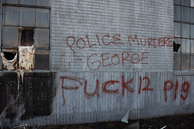 Ein Gebäude mit Graffiti, das "Polizei Mord George Fuck 12 P19" auf der Seite trägt, mit Fenstern und diversen Gegenständen vorne drauf.