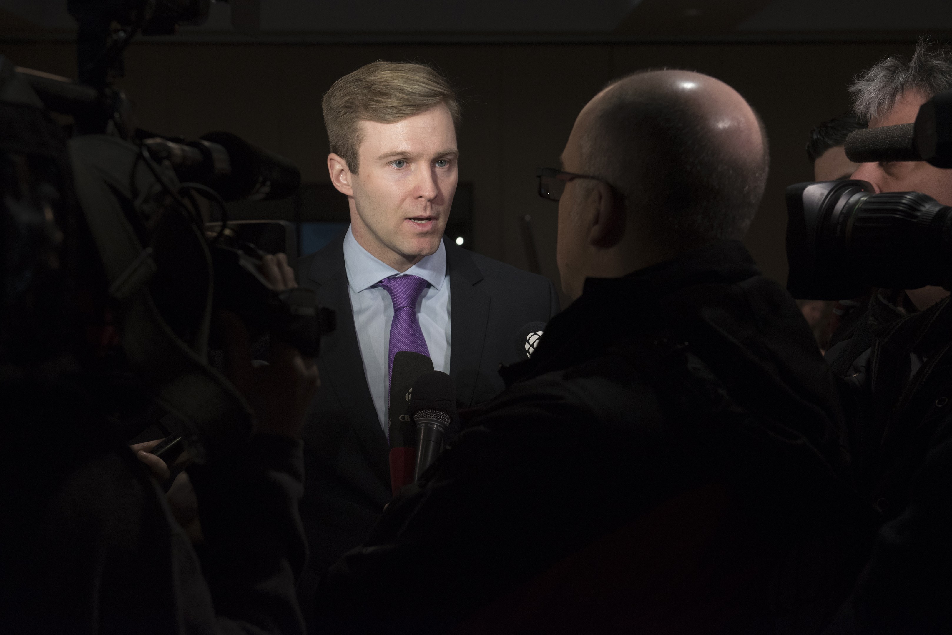 Ein Mann im Anzug mit Brille spricht in ein Mikrofon, während zwei Kameramänner ihn filmen.