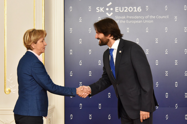 Bundeskanzlerin Angela Merkel und Bundespräsident Joachim Gauck schütteln sich die Hände vor einer Wand mit einem Banner "EU-Gipfel" und einer Tür im Hintergrund, beide lächeln.