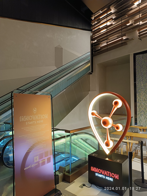 Großes Schild in der Mitte eines Gebäudes mit einer Treppe im Hintergrund, Tische und Stühle auf der rechten Seite und eine Tafel mit "Innovation beginnt hier" auf der linken Seite, was auf die HSTP20 Expo hinweist.