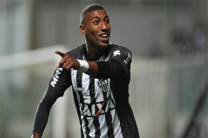 Ein Fußballspieler in einem schwarz-weißen gestreiften Trikot feiert mit einem Lächeln nach einem Tor, der Hintergrund ist unscharf.