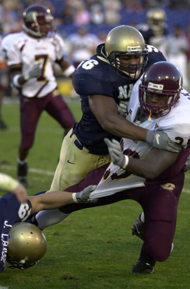 Zwei Fußballspieler in Sportkleidung und Helmen, einer greift den anderen auf dem Feld an.
