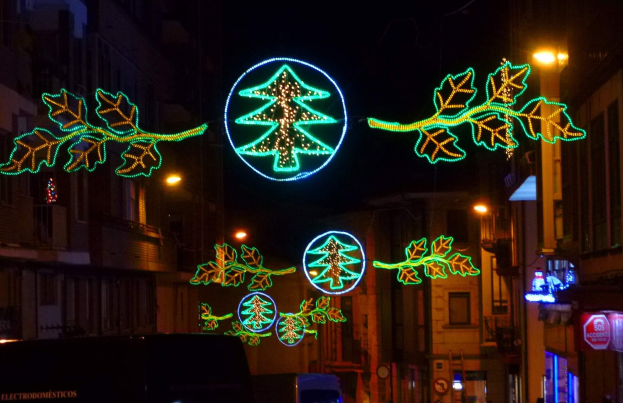 Eine festlich geschmückte Stadtstraße mit Weihnachtslichtern in Form von Blättern, mit fahrenden Fahrzeugen und Gebäuden auf beiden Seiten.