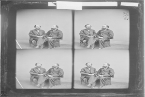 Schwarzes und weißes Foto einer Gruppe von Männern in Anzügen, die in Stühlen sitzen, die in einem Halbkreis angeordnet sind, wobei einige in die Kamera schauen und andere nicht