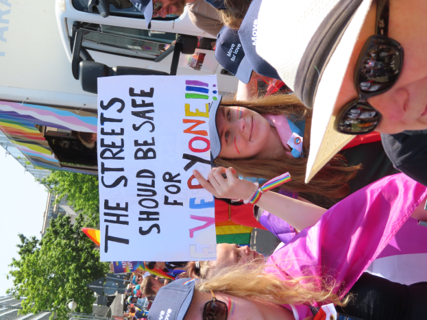 Eine Gruppe von Menschen steht vor einem Lkw und hält ein Schild hoch, auf dem "Die Straßen sollten sicher sein" steht. Einige tragen Mützen und Schutzbrillen, andere halten Schilder. Im Hintergrund sind Bäume, Gebäude und ein klarer blauer Himmel zu sehen.