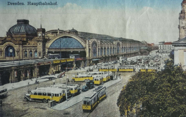 Schwarz-weiß-Postkarte des Dresdner Hauptbahnhof Bahnhofs in Deutschland, zeigt eine belebte Straßenszene mit Fahrzeugen, Fußgängern, Bäumen, Gebäuden und einem bewölkten Himmel.